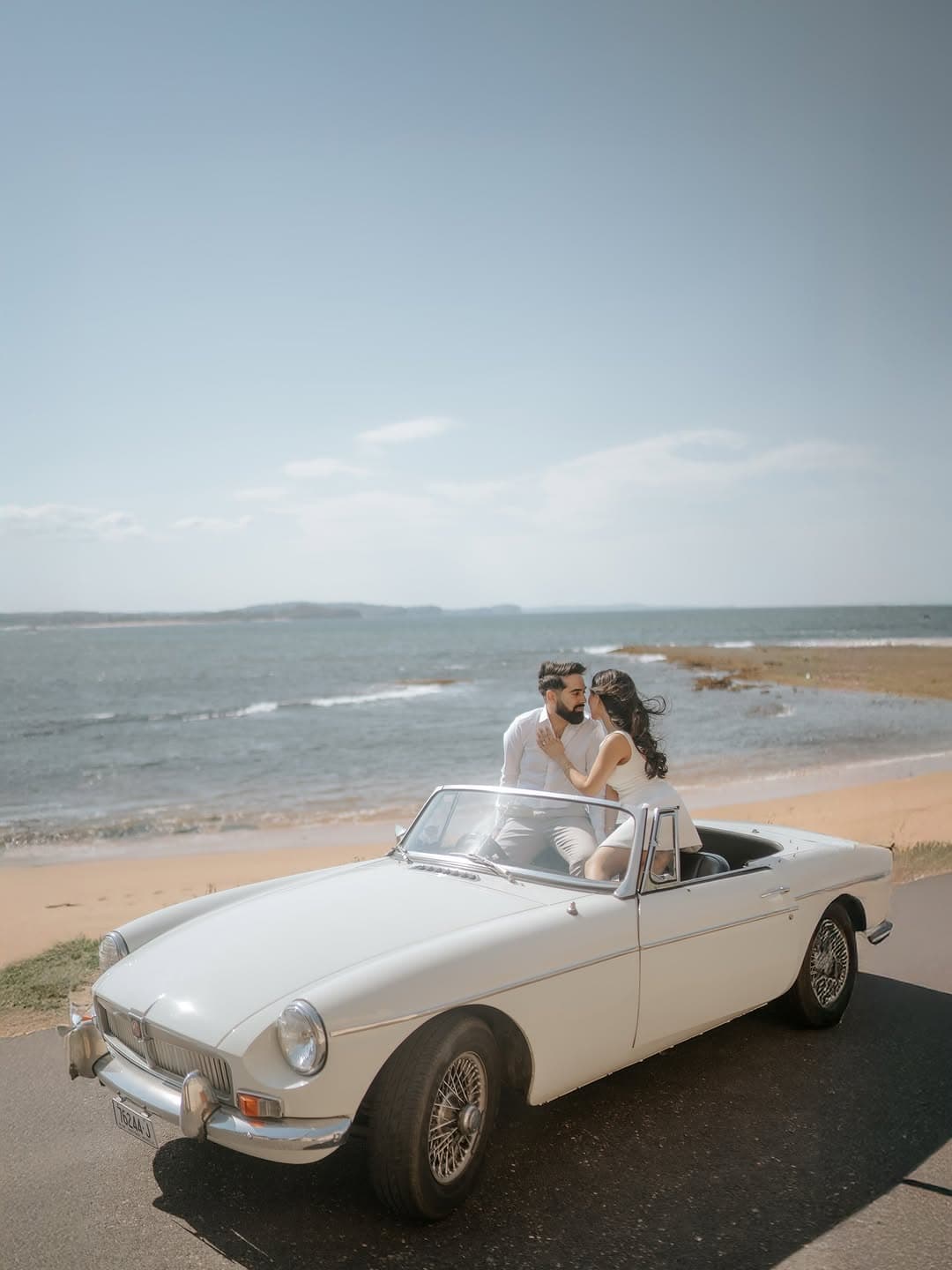 Bridal portrait — couple with vintage MG convertible by the sea
